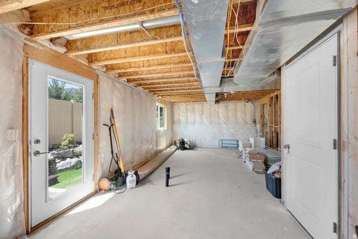 Unfinished lower level with exposed wooden joists and ductwork, featuring a glass-paneled exterior door, insulated walls, an additional window, and a solid interior door