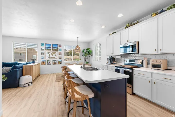 Open-concept living space featuring a kitchen with white cabinetry, stainless steel appliances, a subway tile backsplash, and an island with seating