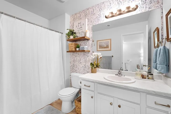 Bathroom featuring wood-finish flooring, a white vanity with an integrated sink, a large mirror, a four-light fixture, and built-in wooden shelving