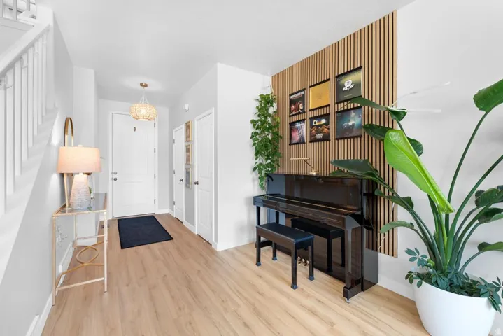 Foyer entrance featuring wood-finish flooring, a contemporary chandelier, a white staircase with wood banister, a paneled accent wall, and a built-in closet