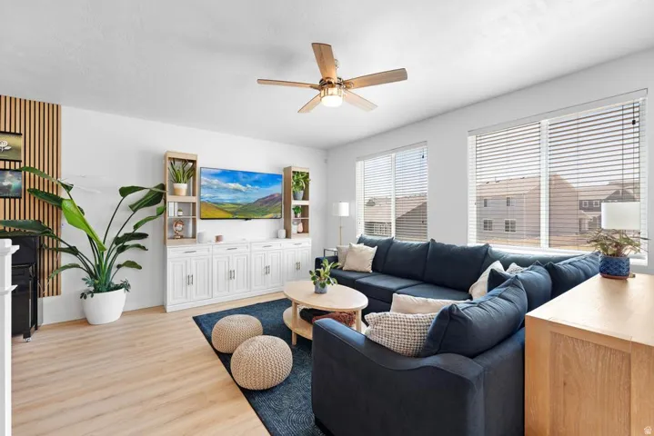 Living area featuring wood-finish flooring, a contemporary ceiling fan, and multiple windows with blinds