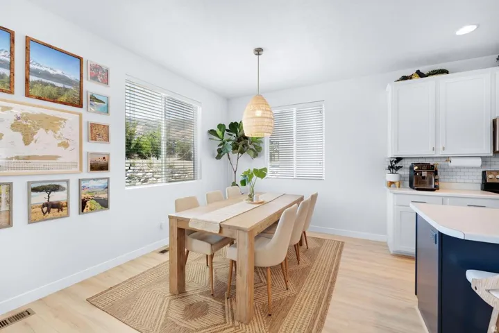 Open-concept dining area featuring light wood-finish flooring, white walls, and a contemporary woven pendant light fixture