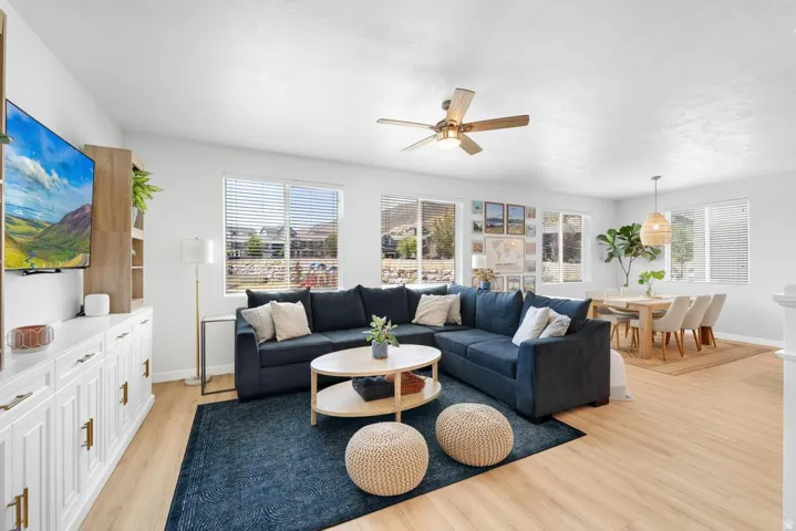 Open-concept living area featuring wood-finish flooring, multiple windows with blinds, a ceiling fan with light fixture, and a built-in entertainment console with storage cabinetry