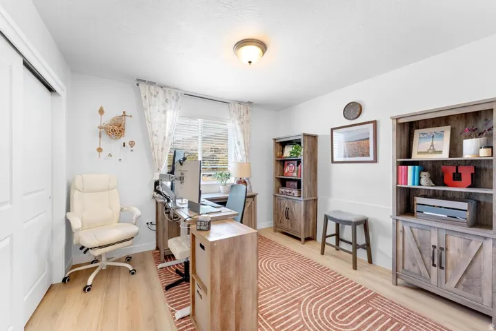 Bedroom featuring white walls, light wood-finish flooring, a window with blinds and sheer curtains, a built-in closet with sliding doors, and a ceiling-mounted light fixture