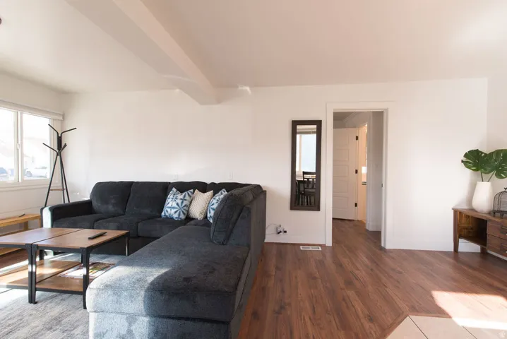 Spacious living area featuring wood-finish flooring, white walls, and a large window providing natural light