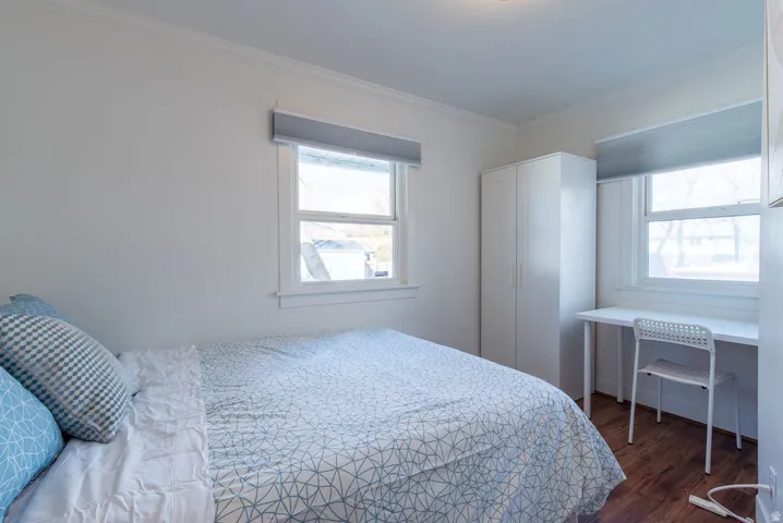 Bright room featuring two windows with roller shades, white trim, and wood-finish flooring