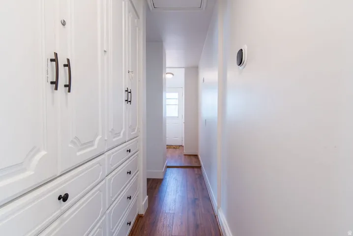 Hallway featuring wood-finish flooring, white built-in cabinetry with panel detailing, black hardware, and a modern wall-mounted thermostat