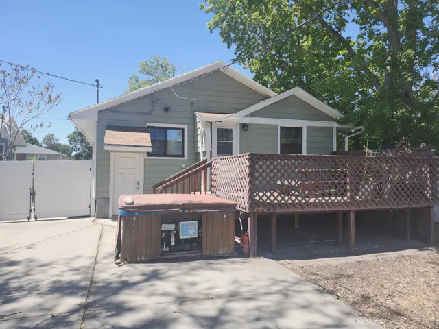 Rear exterior featuring a spacious elevated wood deck with lattice railing, an adjoining concrete patio, a private side entrance, and a white vinyl fence