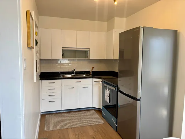 Compact kitchen featuring white cabinetry, dark countertops, a stainless steel refrigerator, a black range, and wood-finish flooring