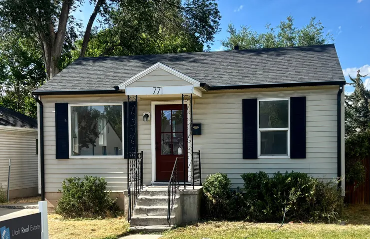 Single-story residence featuring light-colored siding, a dark asphalt shingle roof, and a prominent front entry with a dark-stained door