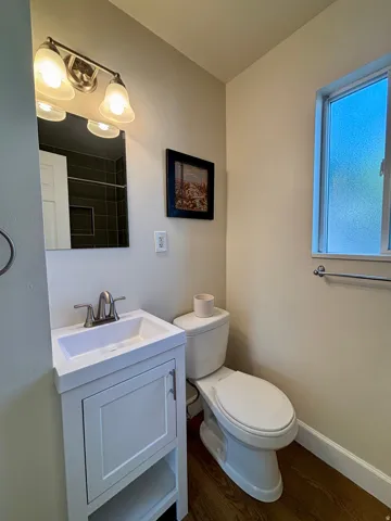 Bathroom featuring a white vanity with integrated sink, brushed nickel faucet, wood-finish flooring, and a frosted window