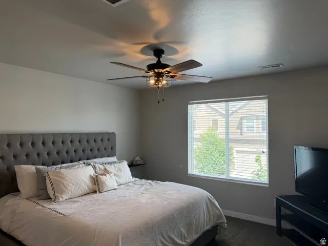 Spacious room featuring neutral paint, soft grey carpeting, a ceiling fan with integrated lighting, and a large window with horizontal blinds