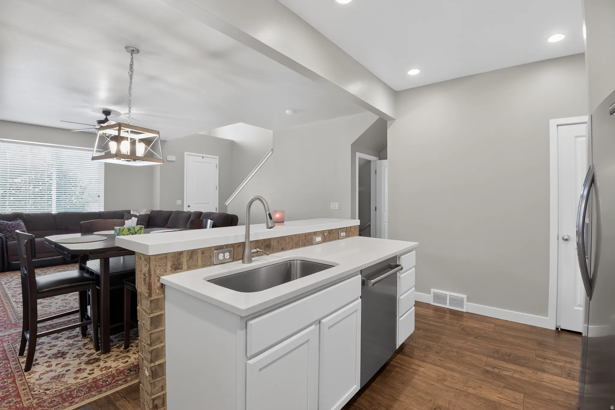 Kitchen island featuring a stainless steel sink, gooseneck faucet, white cabinetry, and a built-in dishwasher
