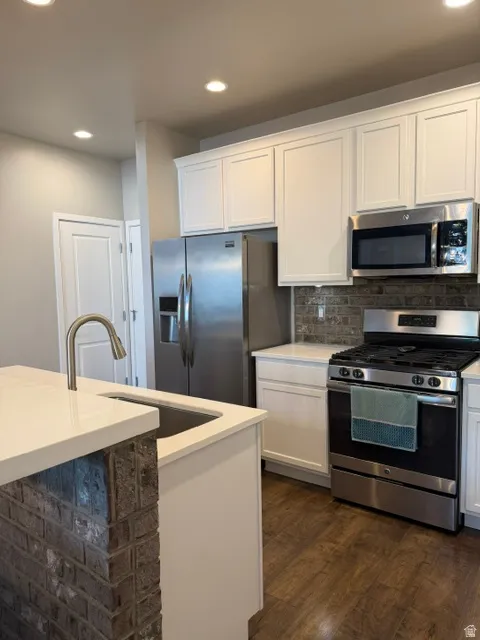 Modern kitchen featuring white cabinetry, stainless steel appliances, a brick-style backsplash, wood-finish flooring, and a kitchen island with integrated sink