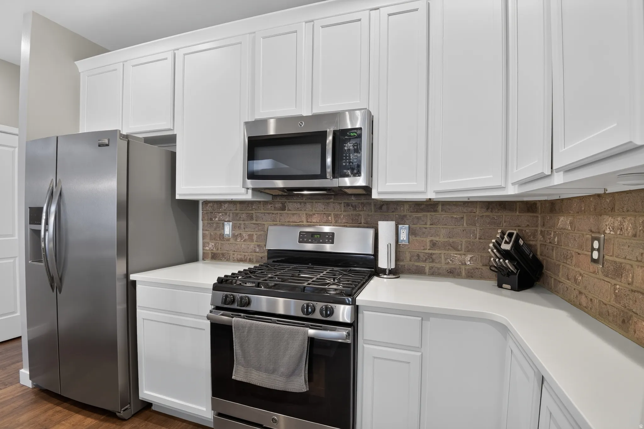 Kitchen featuring white cabinetry, stainless steel appliances, light-colored countertops, brick-patterned backsplash, and wood-finish flooring