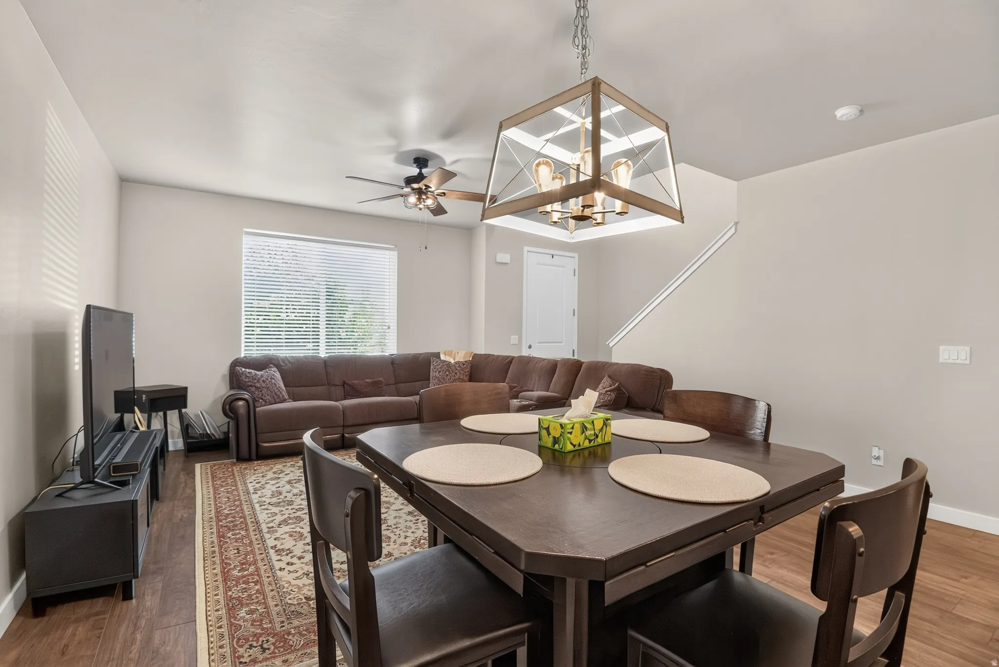Open-concept living area featuring wood-finish flooring throughout, a dining area with a modern chandelier, and a living space with a ceiling fan