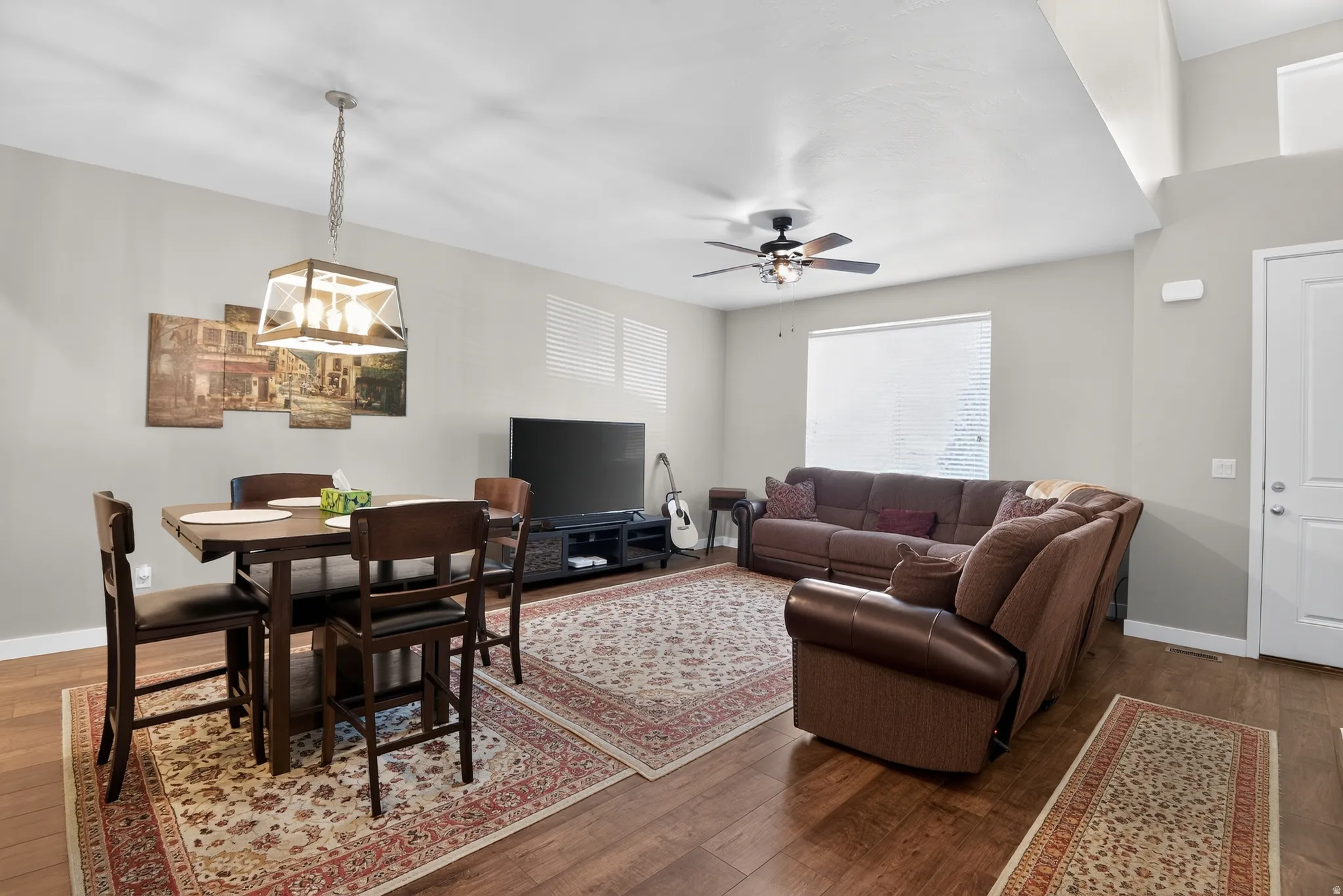 Open-concept living space featuring wood-finish flooring, a contemporary chandelier, a ceiling fan, and a transom window