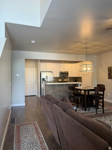 Open-concept living area with wood-finish flooring, a kitchen featuring light cabinetry, stainless steel appliances, and a breakfast bar with brick-style detailing