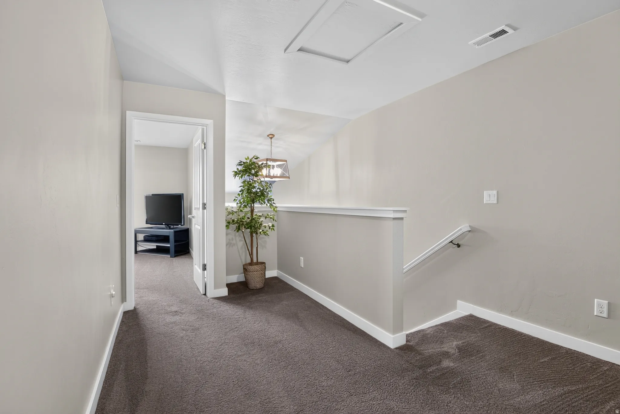 Upper-level hallway featuring neutral wall paint, dark carpet flooring, and white baseboards