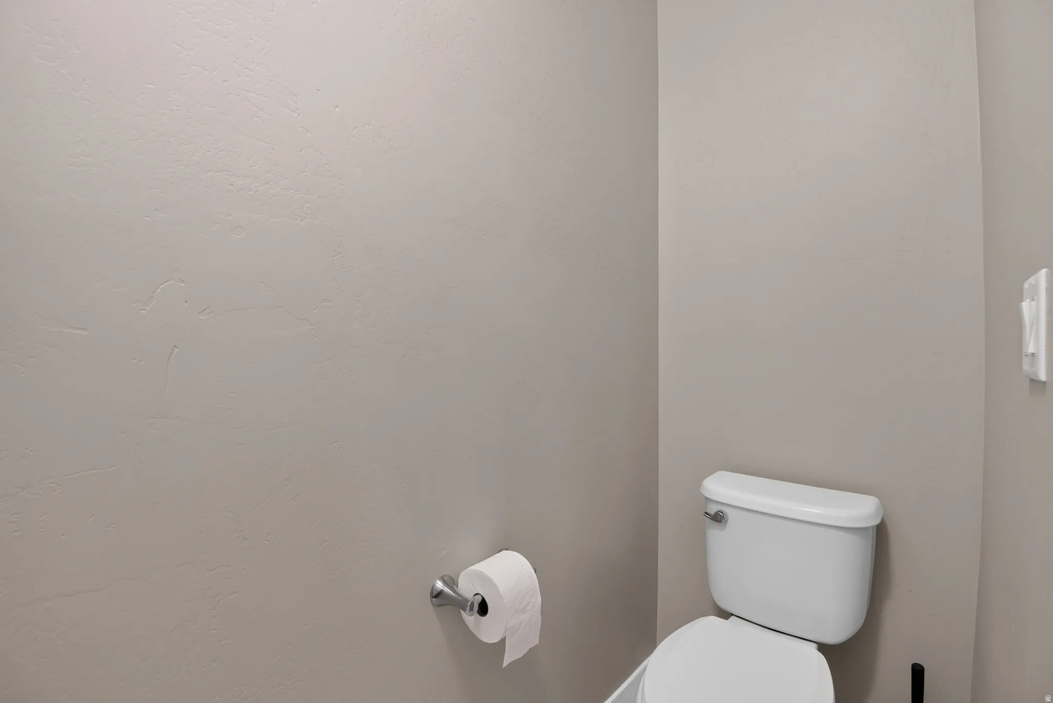 White two-piece toilet with chrome flush lever, set against neutral-toned walls