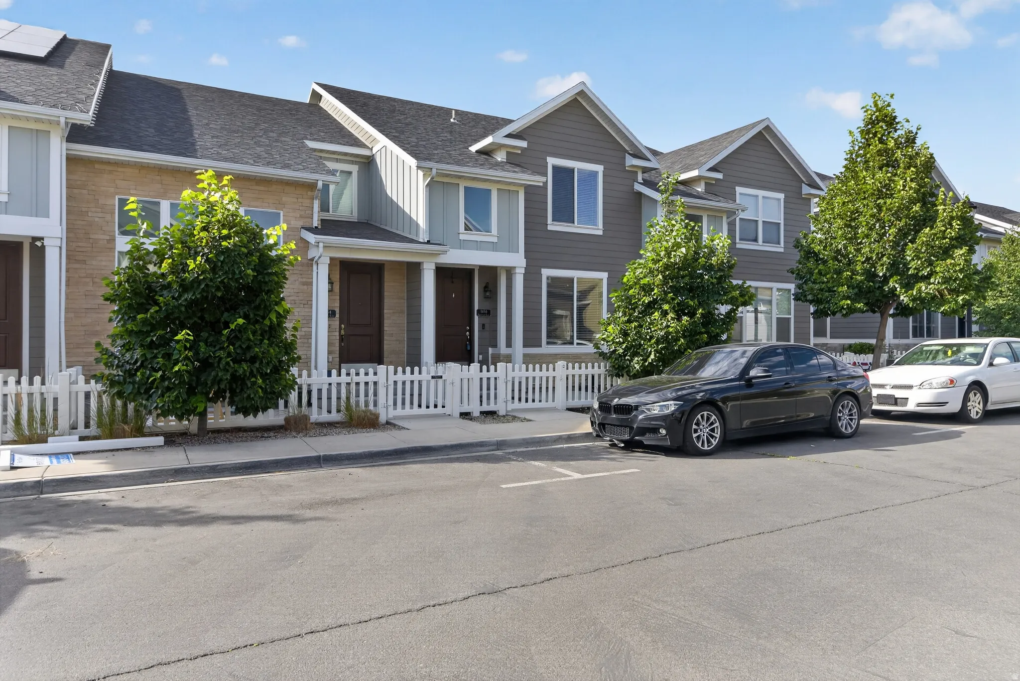 Row of townhomes featuring varied siding finishes, white picket fencing, and mature landscaping