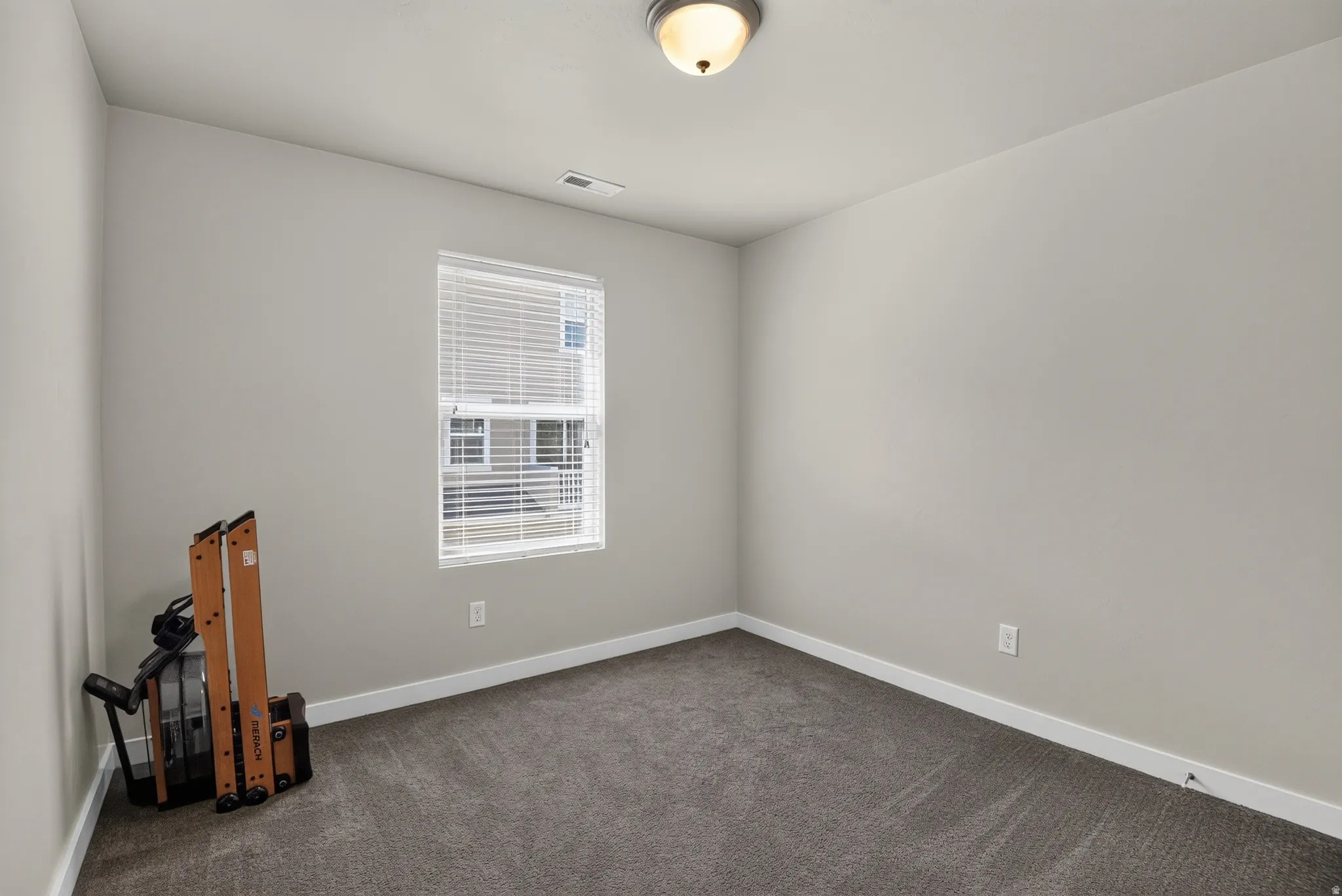 Carpeted room featuring a single window with blinds, light gray walls, white baseboards, and a flush mount ceiling light fixture