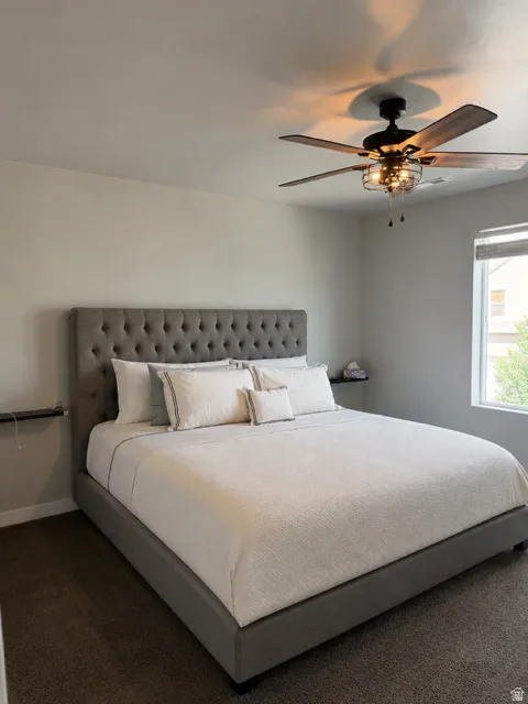 Carpeted room featuring a ceiling fan with integrated lighting, a window with an interior shade, and a wall-mounted shelf