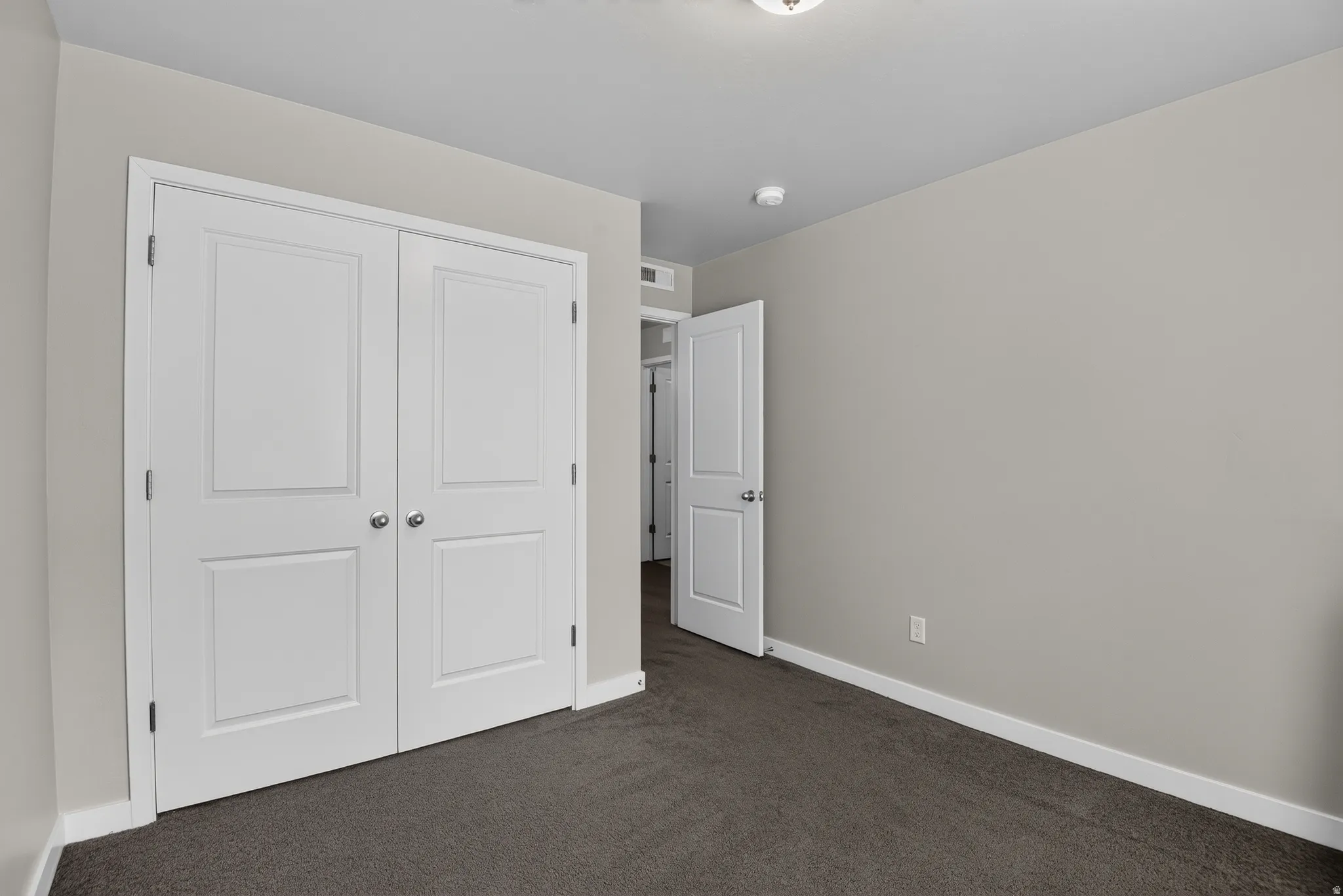 Room featuring neutral wall tones, gray carpeting, white trim, and a double-door closet