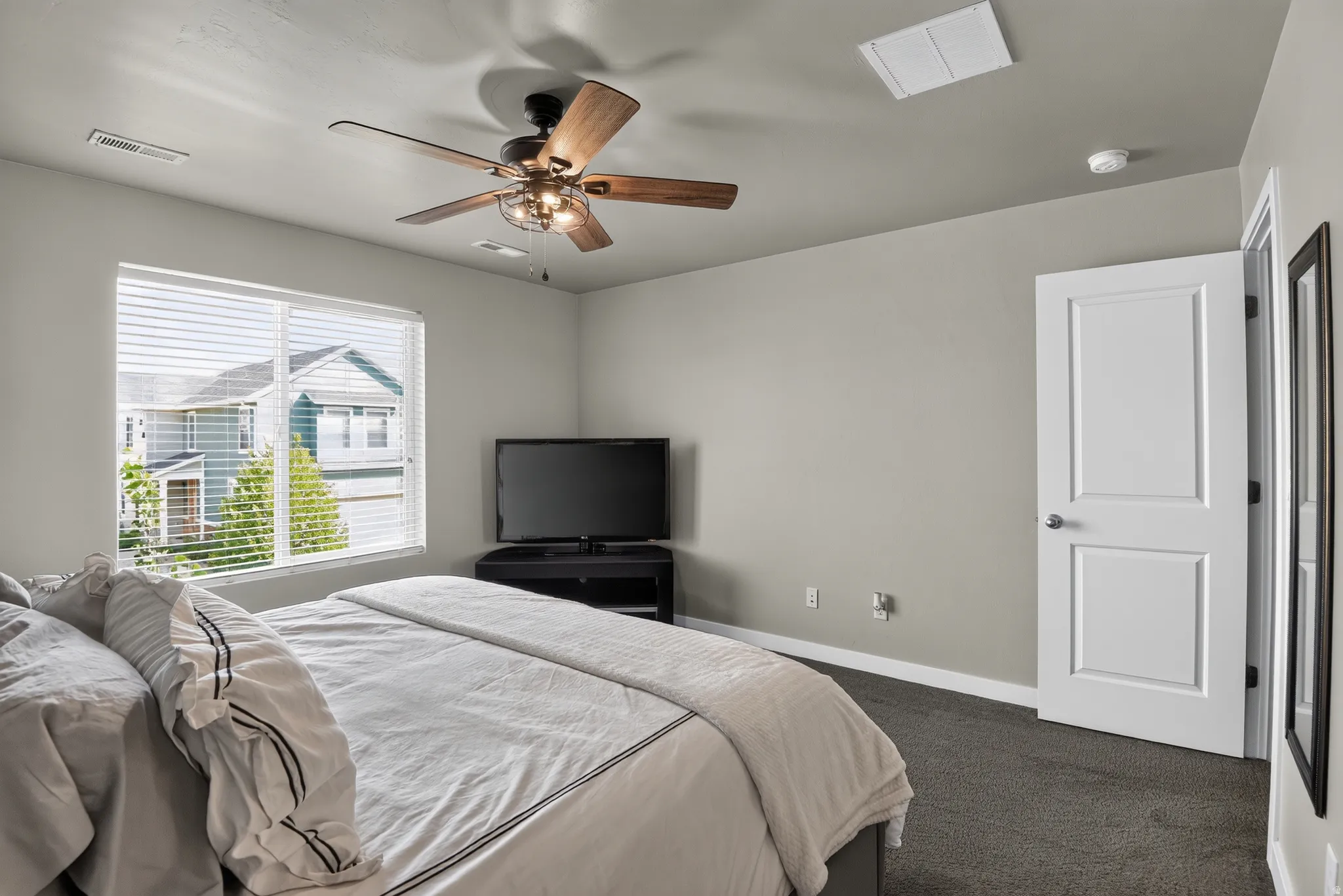 Carpeted room featuring a ceiling fan with integrated lighting, a large window with horizontal blinds, and a paneled white door with silver hardware