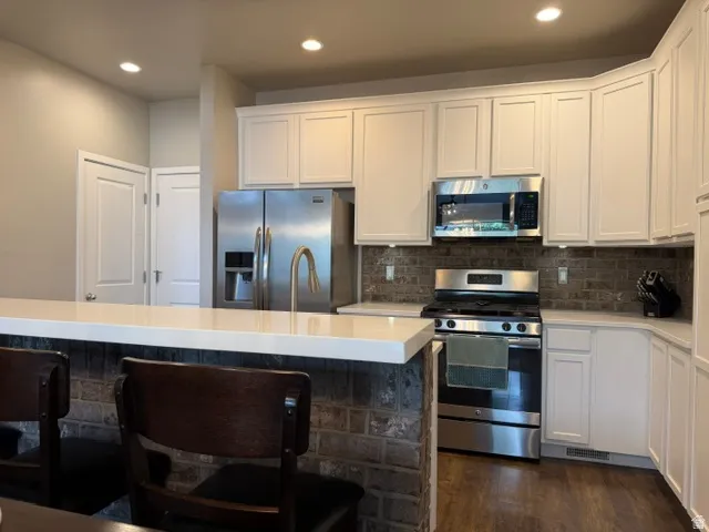 Contemporary kitchen featuring a breakfast bar with stone veneer base, white shaker cabinetry, stainless steel appliances, and wood-finish flooring