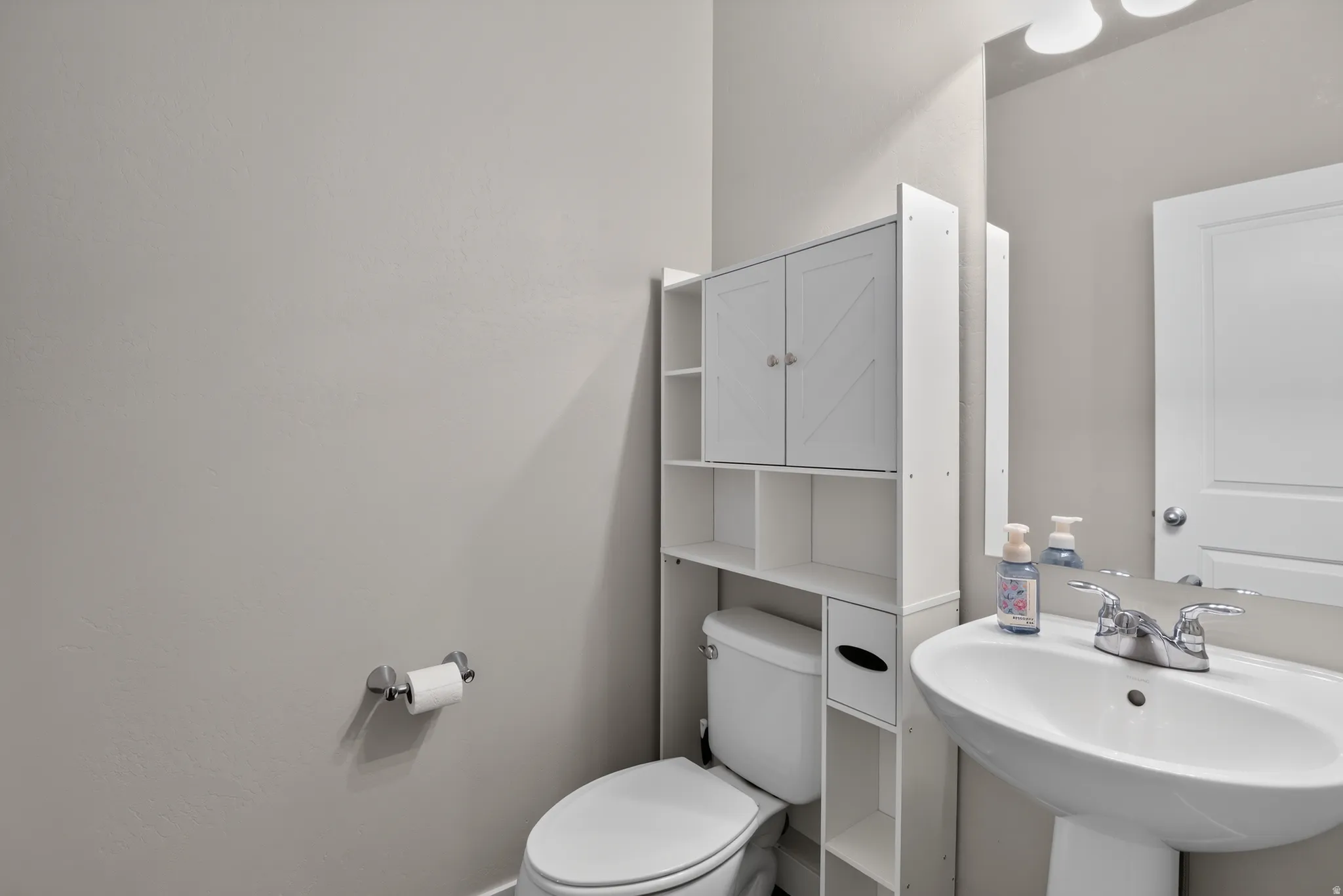 Pedestal sink with chrome fixtures and an overhead vanity light