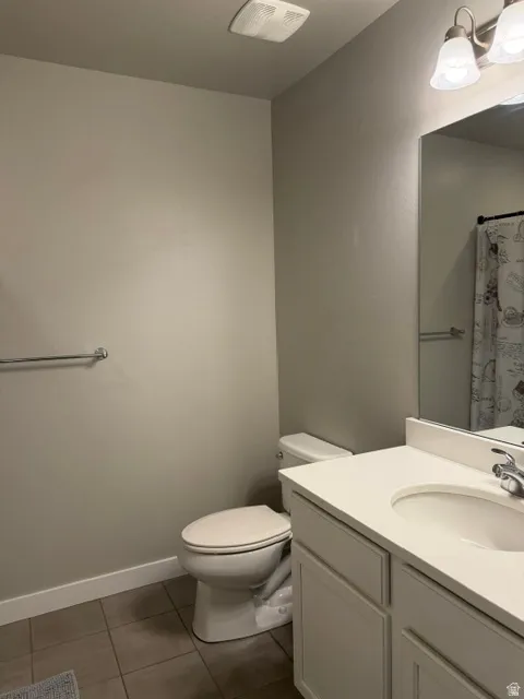 Bathroom featuring a single vanity with a white countertop and integrated sink, a built-in toilet, and tile flooring