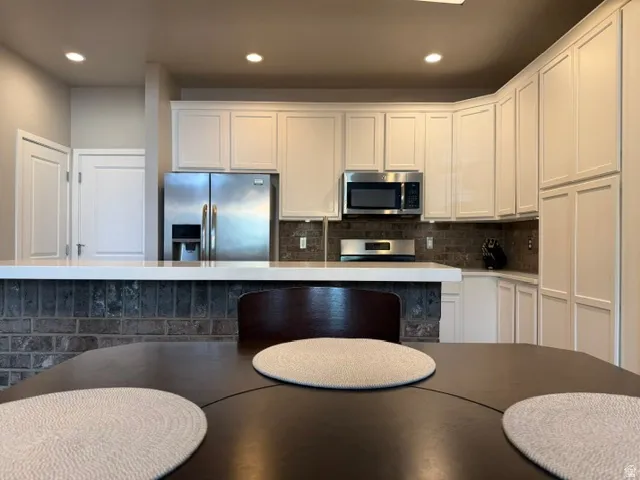 Modern kitchen featuring white cabinetry, stainless steel appliances, a brick-textured island base, and a light-toned countertop