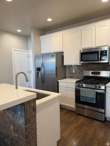Modern kitchen featuring white cabinetry, stainless steel appliances, a brick-style backsplash, wood-finish flooring, and a kitchen island with integrated sink