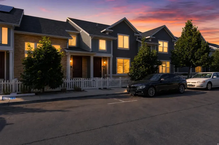 Townhome exterior featuring brick and siding facades, gabled roofs, solar panels, mature trees, and a white picket fence