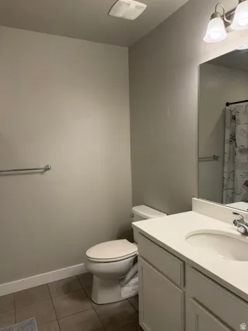 Bathroom featuring a single vanity with a white countertop and integrated sink, a built-in toilet, and tile flooring