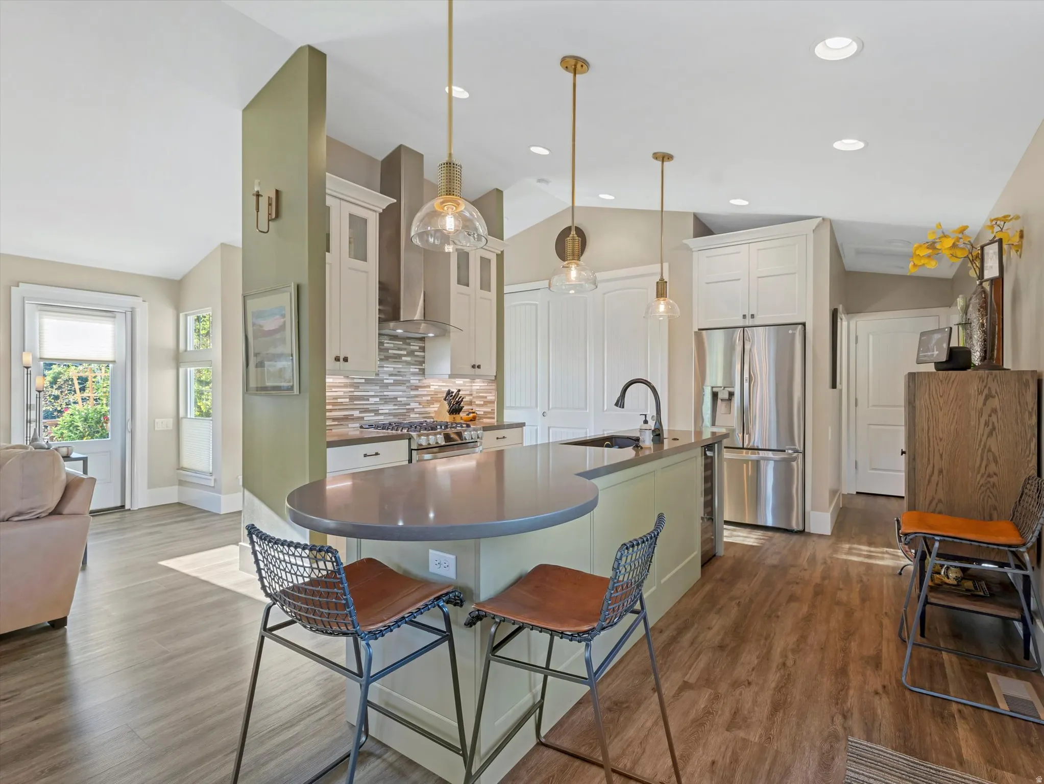 Kitchen featuring lofted ceiling, stainless steel appliances, decorative backsplash, white cabinetry, and wall chimney exhaust hood