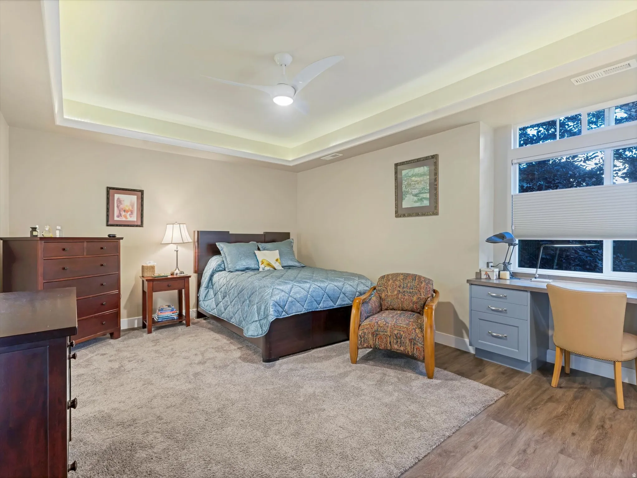 Bedroom featuring ceiling fan, a tray ceiling, an office area, and wood finished floors