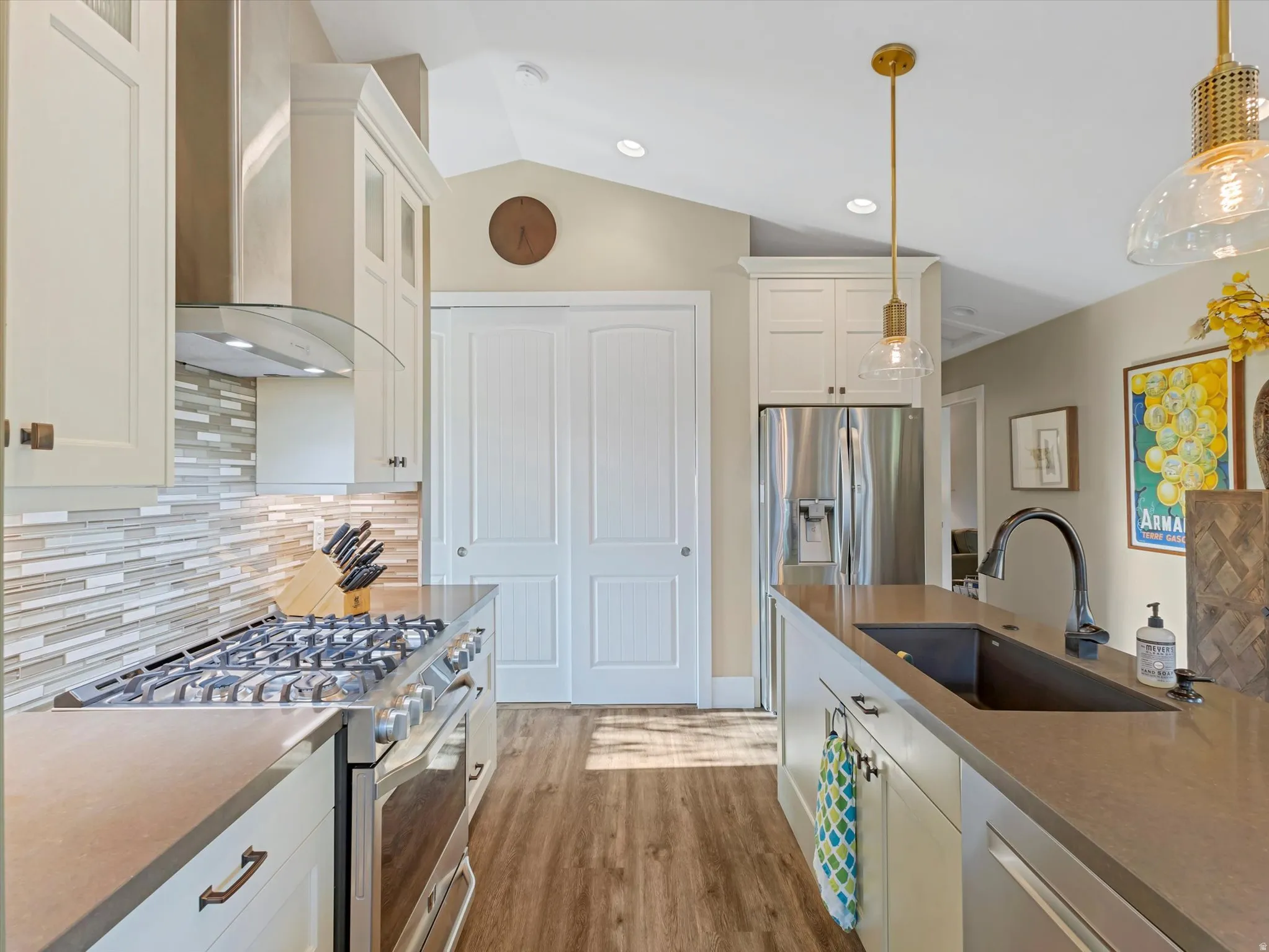 Kitchen with decorative backsplash, appliances with stainless steel finishes, wall chimney exhaust hood, lofted ceiling, and white cabinets