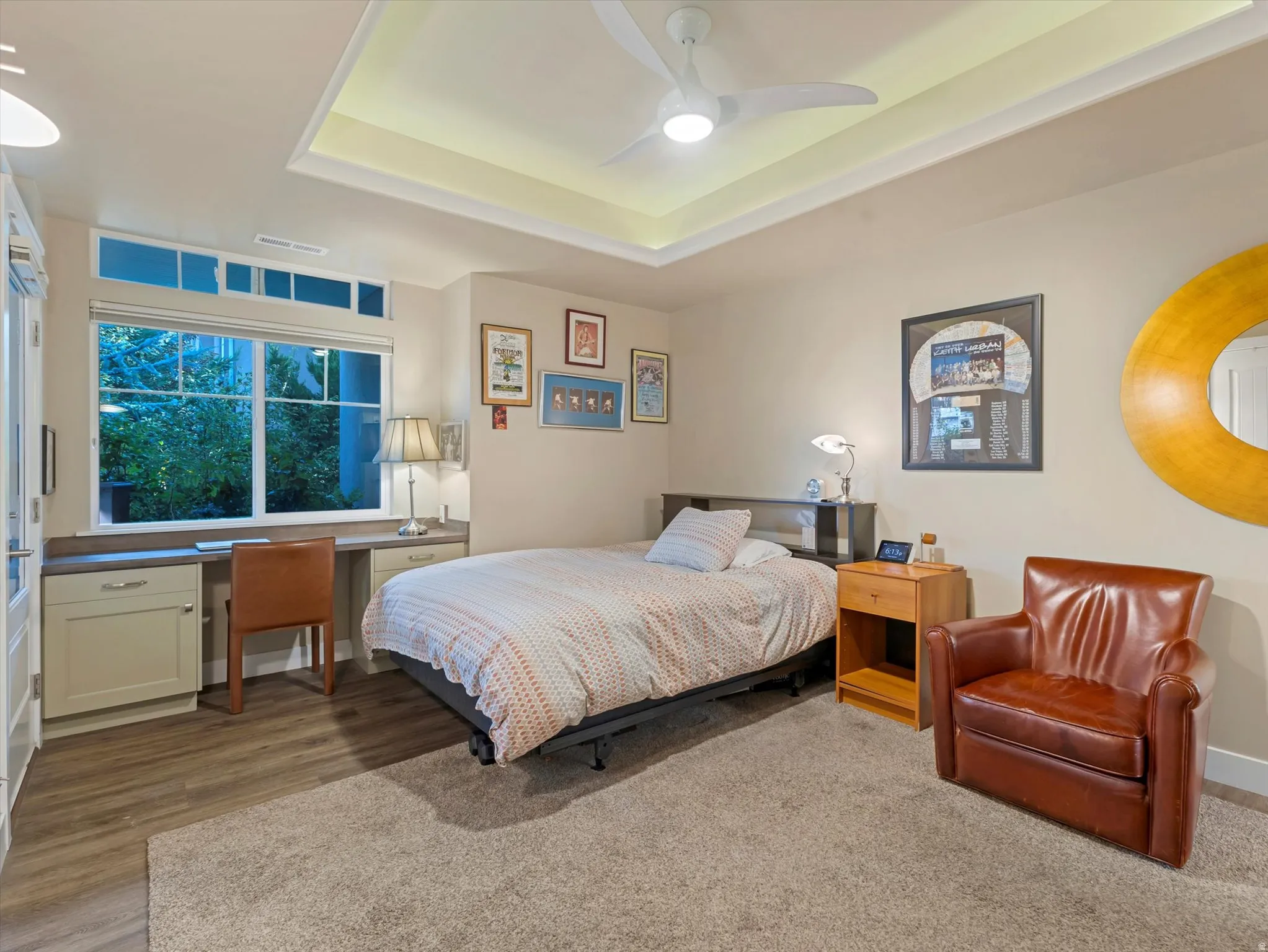 Bedroom featuring built in desk, a tray ceiling, ceiling fan, and light wood-style flooring