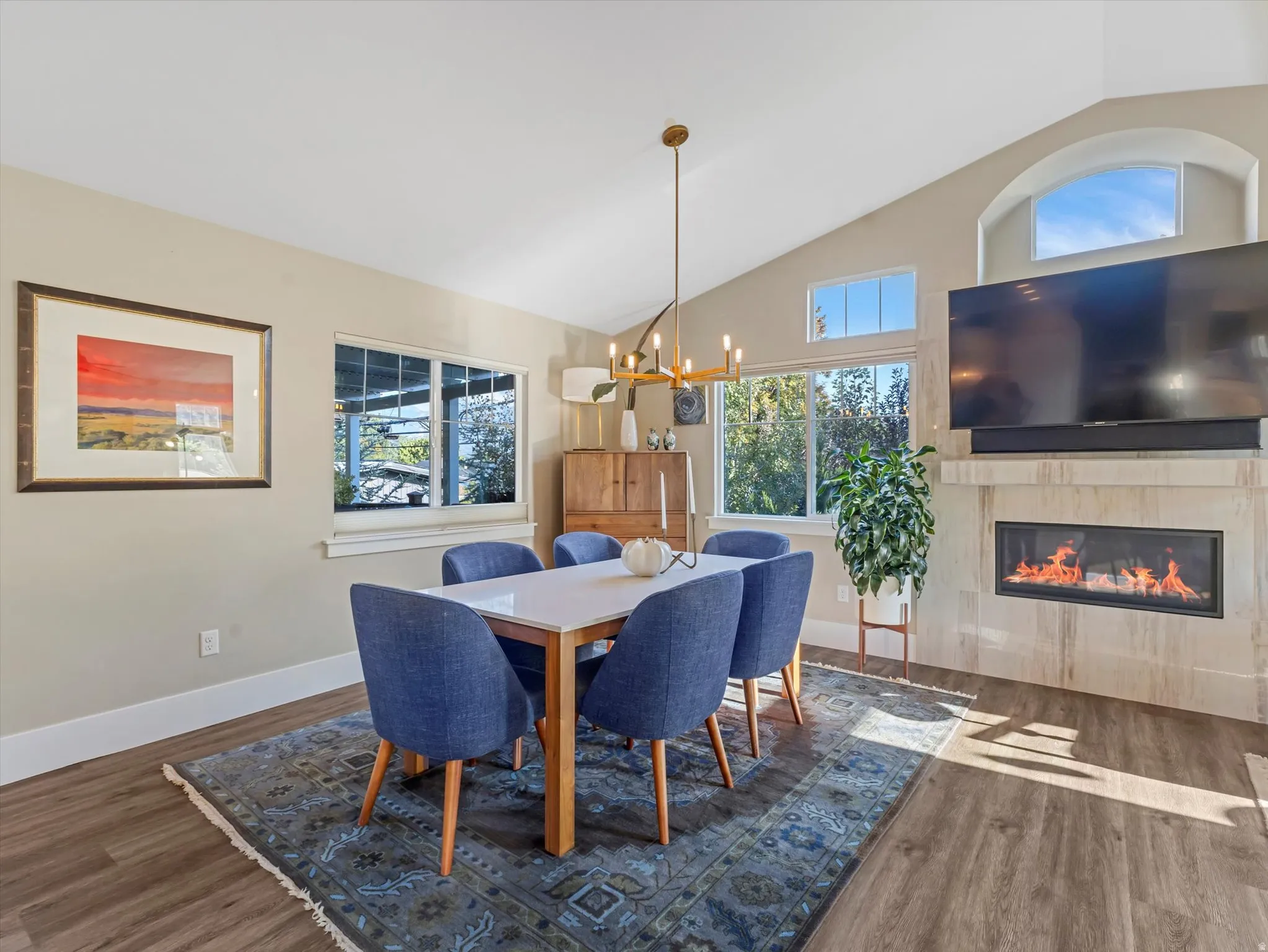 Dining room with a tiled fireplace, high vaulted ceiling, wood finished floors, and a chandelier