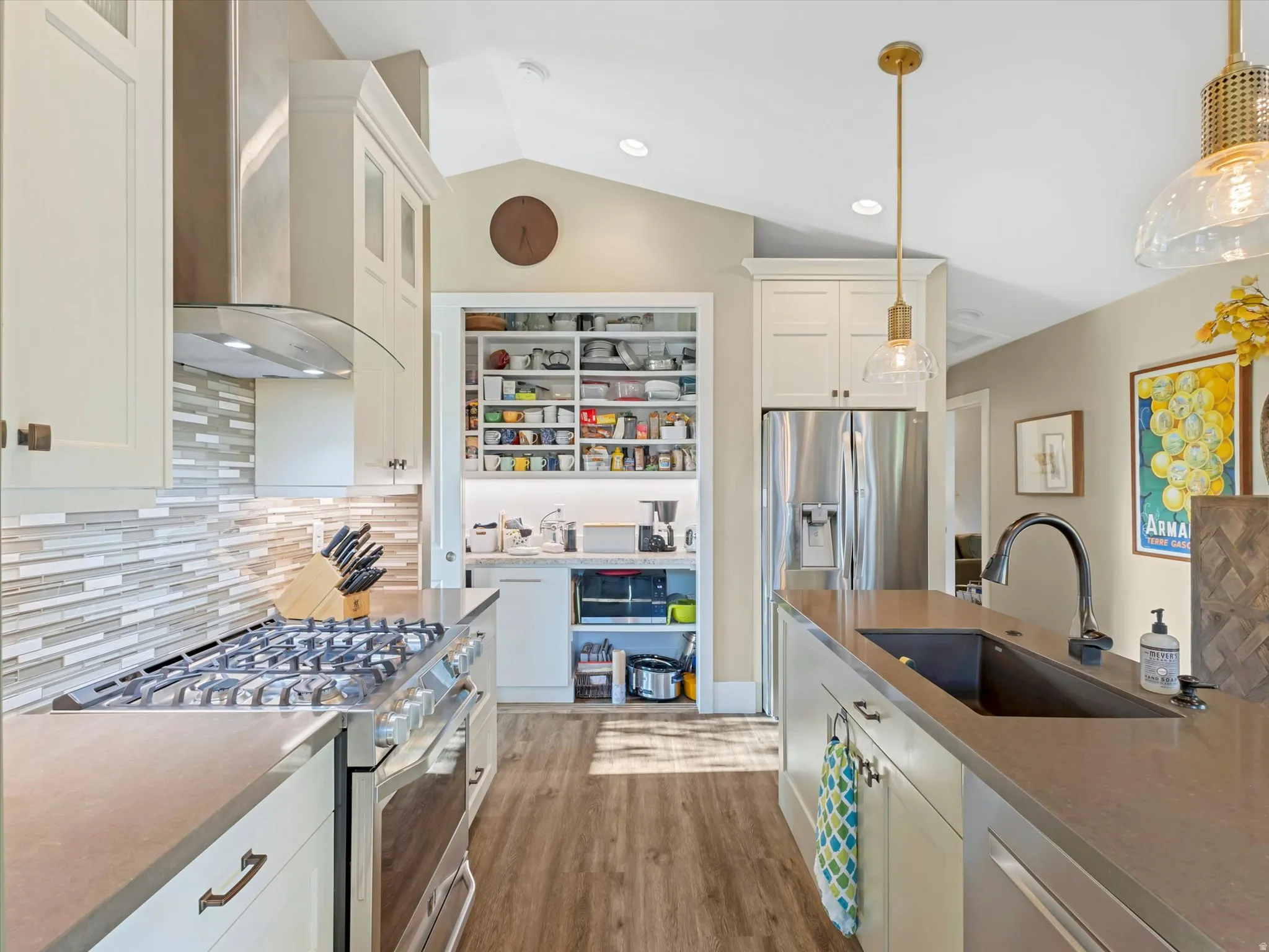 Kitchen featuring backsplash, stainless steel appliances, white cabinetry, wall chimney range hood, and lofted ceiling
