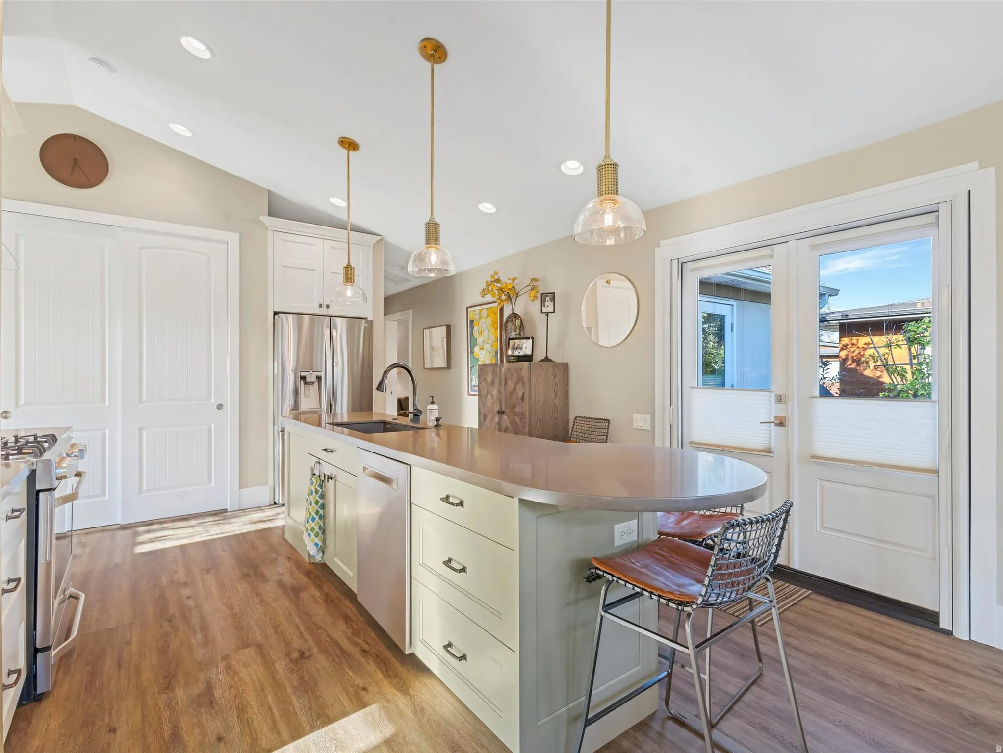 Kitchen with white cabinets, light wood-style flooring, decorative light fixtures, lofted ceiling, and a breakfast bar area