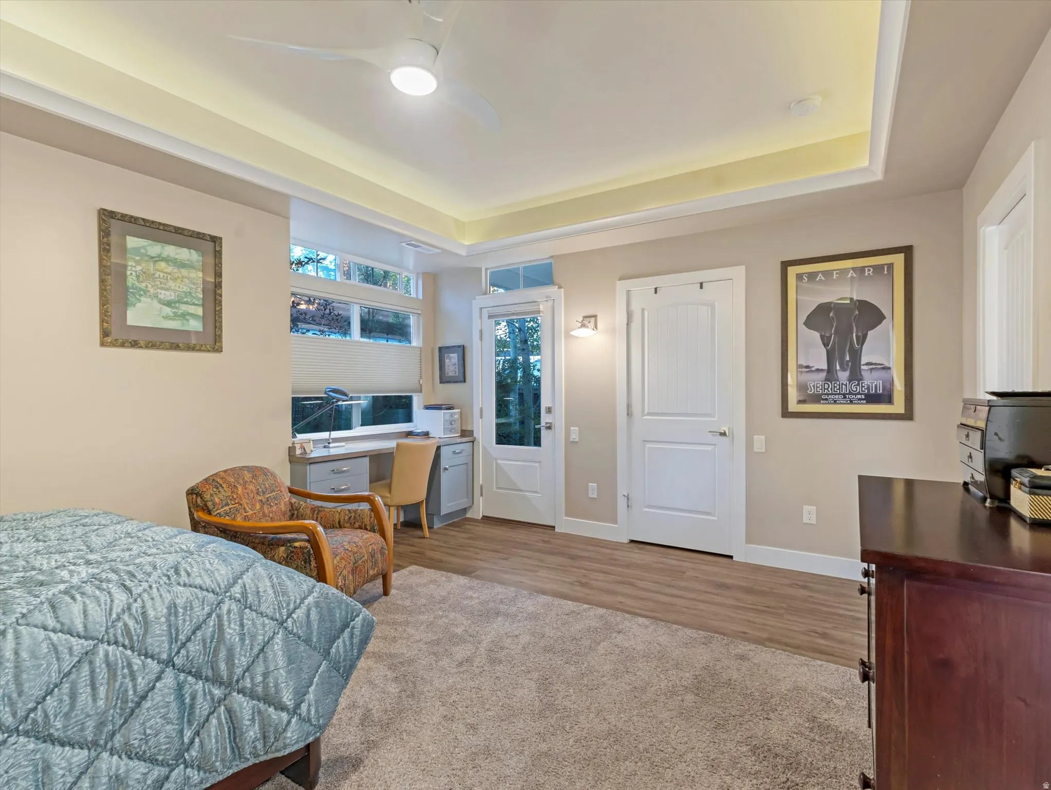 Bedroom with an office area, a raised ceiling, ceiling fan, and light wood-style flooring
