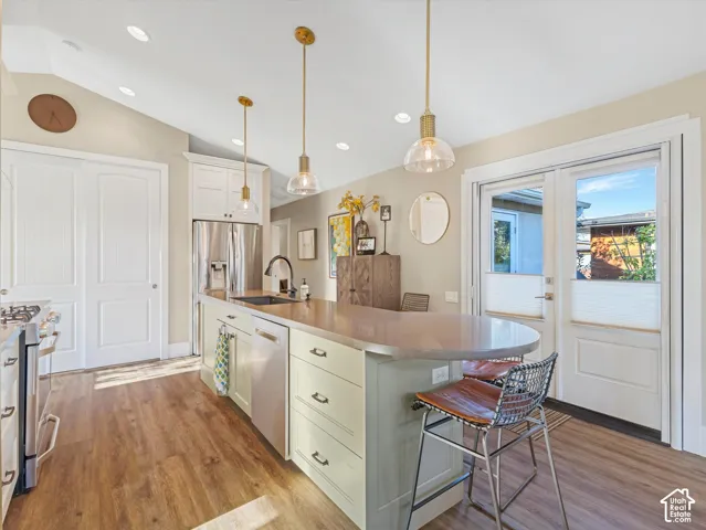 Kitchen with white cabinets, light wood-style flooring, decorative light fixtures, lofted ceiling, and a breakfast bar area