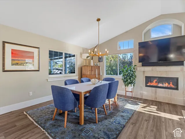 Dining room with a tiled fireplace, high vaulted ceiling, wood finished floors, and a chandelier