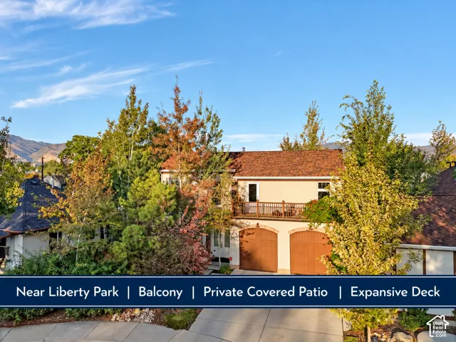 Two-car garage with arched doors, upper-level balcony with wood railing, and mature landscaping