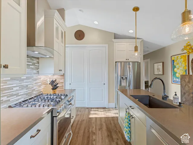 Kitchen with decorative backsplash, appliances with stainless steel finishes, wall chimney exhaust hood, lofted ceiling, and white cabinets