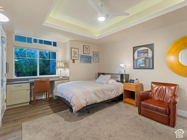 Bedroom featuring built in desk, a tray ceiling, ceiling fan, and light wood-style flooring