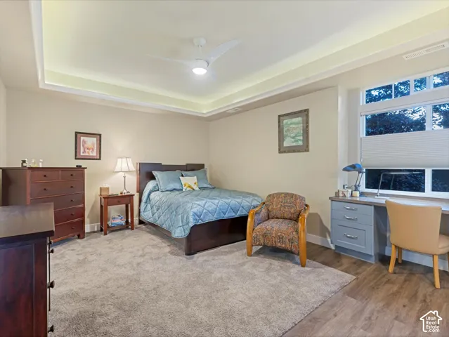 Bedroom featuring ceiling fan, a tray ceiling, an office area, and wood finished floors